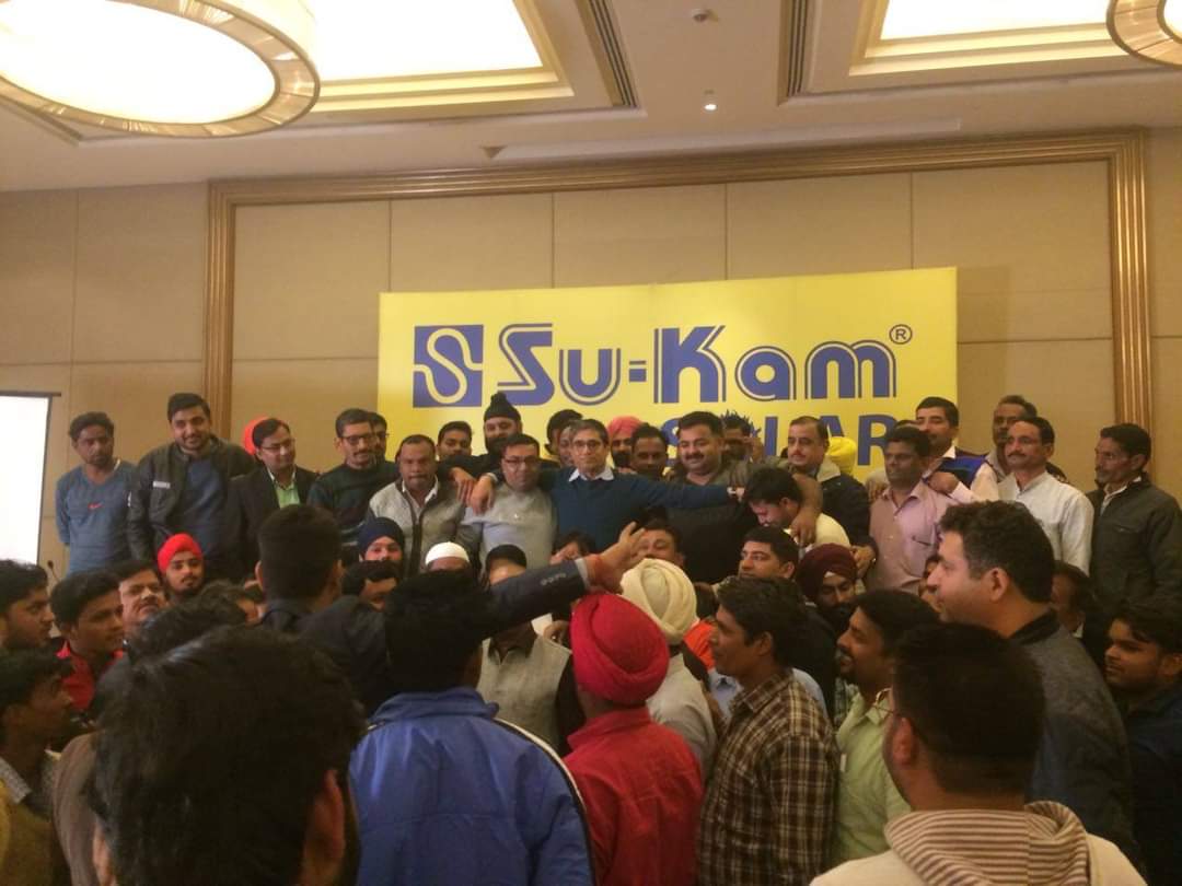 Dealers gathered closely around Kunwer Sachdev in front of a large yellow Su-Kam Solar board